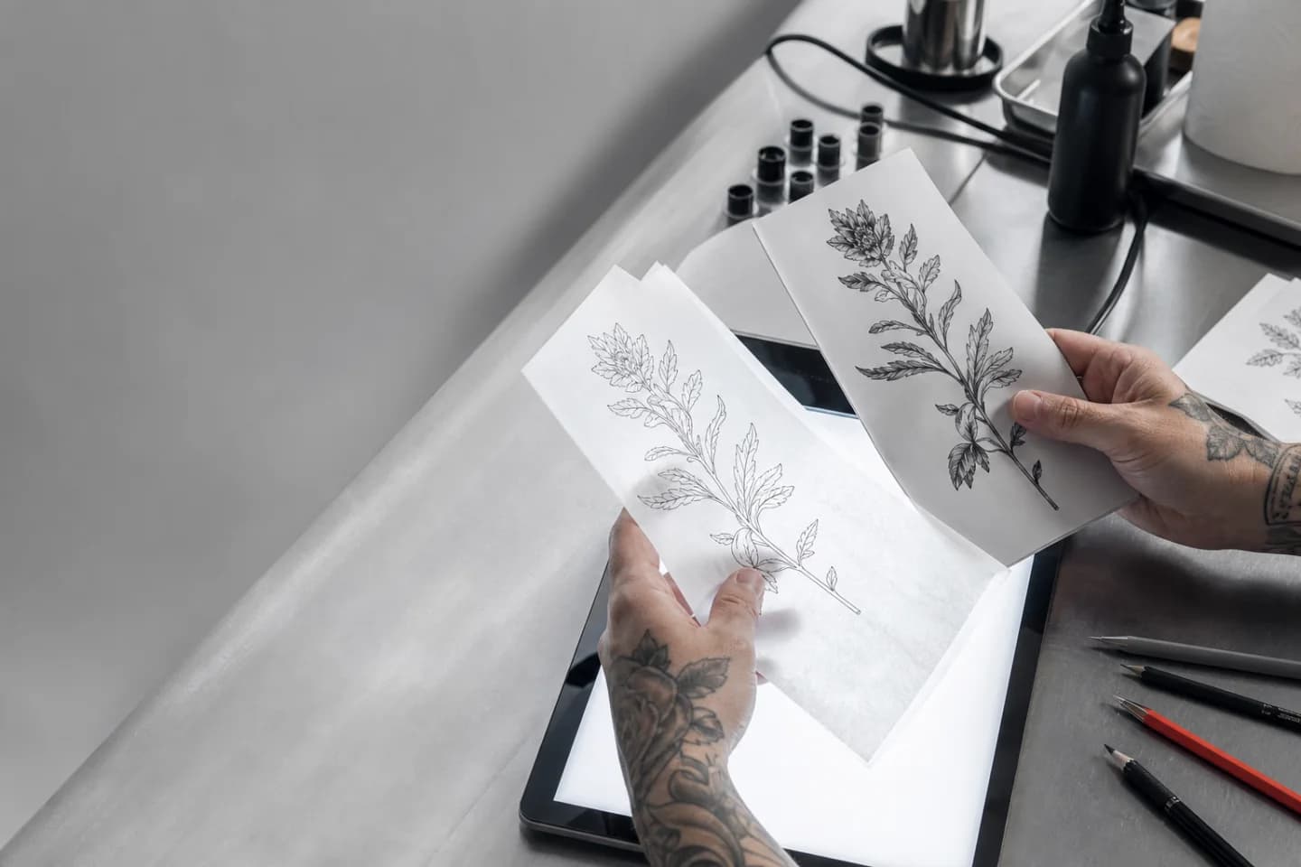 Tattoo artist comparing botanical reference art with clean stencil linework